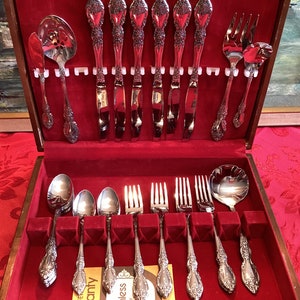 May include: A wooden box with a red velvet interior containing a set of silver cutlery. The cutlery includes knives, forks, spoons, and serving utensils. The box is open and the cutlery is arranged in rows.