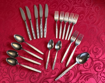 Puede incluir: Un juego de cubiertos de acero inoxidable, que incluye cucharas, tenedores y cuchillos, dispuestos sobre un mantel rojo estampado. Los cubiertos tienen mangos decorativos. La imagen muestra un juego de comedor completo.
