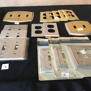 May include: A collection of 10 light switch and outlet covers in gold and brushed nickel finishes. The covers are packaged in plastic bags and boxes. The covers are labelled with the numbers 3 and 6.