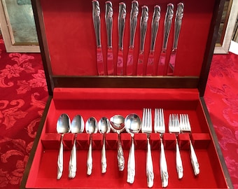 May include: A wooden box with a red velvet interior containing a set of silverware. The silverware includes knives, forks, and spoons. The silverware is arranged in a neat and organized manner.