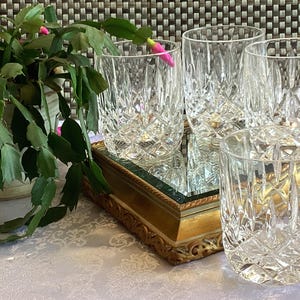 May include: Four clear glass tumblers with a cut-glass design, arranged on a gold-coloured tray with a mirrored surface.
