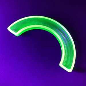 Può includere: Un oggetto curvo verde neon con un bordo bianco, su uno sfondo viola scuro. L'oggetto ha un aspetto liscio e lucido e una forma semicircolare. Il colore verde vibrante è il punto focale.