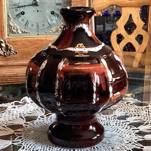 May include: A decorative, vintage ceramic vase with a dark brown base and a bulbous body. The vase features a glossy finish with a pattern of brown, red, and white vertical stripes. The vase is likely used for home decor.