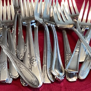 Puede incluir: Una colección de tenedores de plata vintage con diseños ornamentados. Los tenedores están dispuestos en un patrón de cruz, mostrando sus intrincados detalles.