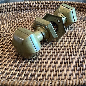 Peut inclure: Deux poignées de porte antiques en laiton avec un design géométrique. Les boutons sont montés sur une plaque hexagonale. La quincaillerie est de couleur laiton vieilli et chaud. Les boutons sont sur un plateau en osier tressé.