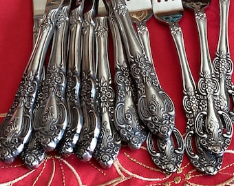 May include: Close-up of a set of ornate silver forks. The forks have detailed floral patterns on the handles. The tines are visible, and the silverware is arranged on a red tablecloth.