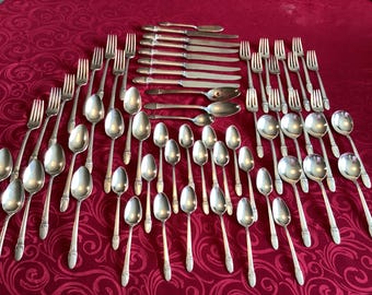 May include: An assortment of silver-colored flatware, including forks, spoons, and knives, arranged on a red patterned tablecloth. The silverware is neatly organized, showcasing a complete set for dining.
