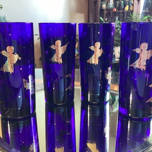 Peut inclure: Quatre verres à boire en verre bleu cobalt avec des silhouettes d'anges dorées et un motif étoilé. Les verres sont sur un plateau argenté.