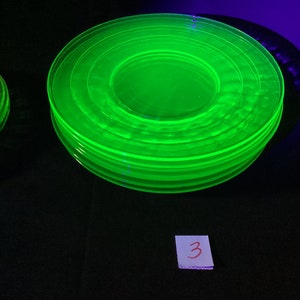 Op de afbeelding: Een stapel van zeven felgroene glazen borden, waarschijnlijk uraniumglas, met het nummer "3" geschreven op een papiertje op de voorgrond.