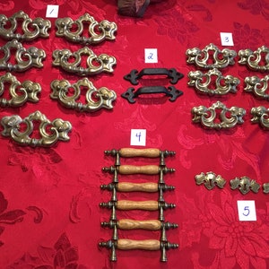 May include: Assortment of 10 antique brass cabinet knobs and pulls, including 6 ornate pulls with a scroll design, 2 simple black pulls, 2 wooden pulls with brass accents, and 2 small ornate brass knobs.