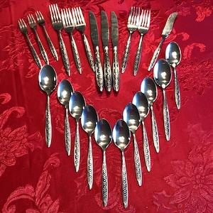May include: A set of silverware arranged in a heart shape on a red tablecloth. The silverware includes forks, spoons, and knives, all with an ornate design.