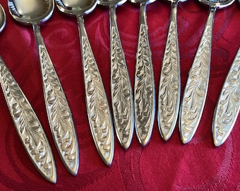 Op de afbeelding: Een set zilverkleurige metalen lepels met een gedetailleerd reliëfpatroon van bladeren en ranken over de lengte van de stelen. De lepels hebben gepolijste, ronde kommen en taps toelopende stelen met een consistente decoratieve textuur.