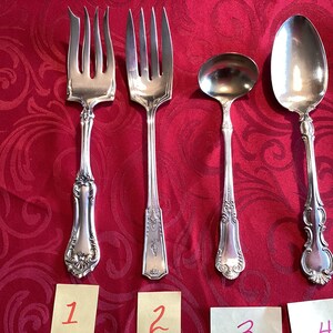 K&ouml;nnte beinhalten: Vier Besteckteile auf einer roten Tischdecke. Das Besteck umfasst eine Gabel, einen L&ouml;ffel, einen Servierl&ouml;ffel und eine Serviergabel.