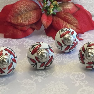 May include: Four white ceramic cabinet knobs with red floral designs and silver accents.