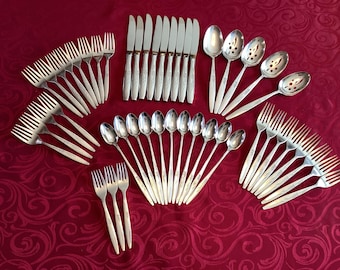 May include: A set of silver flatware, including forks, knives, spoons, and serving utensils. The flatware is arranged in a circular pattern on a red background.