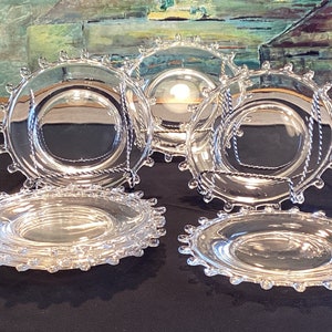 May include: Set of eight clear glass dessert plates with a beaded edge. The plates are stacked in two groups of four.