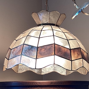 May include: A dome-shaped pendant lamp featuring a scalloped edge and a geometric grid pattern. The shade is constructed from translucent, iridescent shell panels with a central horizontal band of darker, mottled brown shell segments.