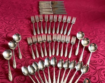 May include: A set of silverware with a silver finish. The set includes forks, spoons, and knives. The silverware is arranged in a fan shape on a red tablecloth.