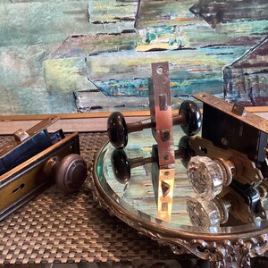 Può includere: Tre pomelli per porte antichi con buchi per le chiavi e piastre. Due pomelli sono neri con una piastra in ottone e un pomello è in vetro trasparente con una piastra in ottone.