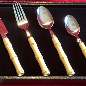 Könnte beinhalten: Ein Set aus vier silberfarbenen Besteckteilen mit Griffen im Bambus-Stil. Das Set enthält ein Messer, eine Gabel und zwei Löffel.