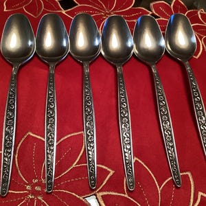 Peut inclure: Six cuillères en argent avec des motifs floraux ornés sur un fond rouge.