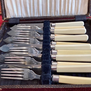Puede incluir: Un juego de ocho tenedores de plata con mangos de marfil en una caja forrada de terciopelo negro. Los tenedores tienen un diseño ornamentado y están en excelente estado.