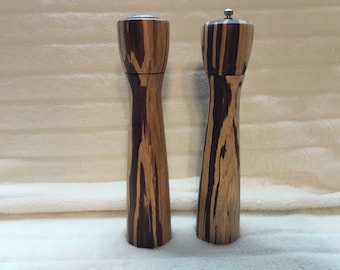 Könnte beinhalten: Ein Set aus zwei Salz- und Pfeffermühlen aus Holz mit einem Muster aus dunkelbraunem und hellem Holz.