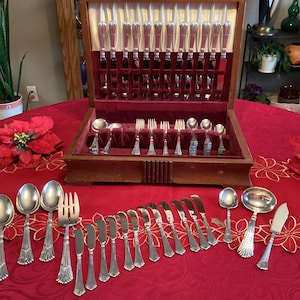 May include: A wooden box containing a set of silver cutlery, including forks, knives, and spoons. The cutlery is arranged in the box in a neat and organised manner. The box is open and the cutlery is visible.