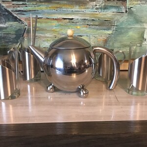 May include: A silver teapot with a round body and three ball feet, along with four matching silver cups with glass inserts.
