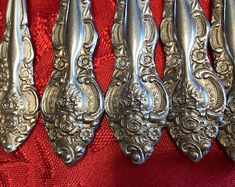 May include: A set of silver-plated, ornate teaspoons with a floral design. The handles are intricately detailed with roses and leaves.