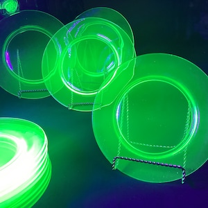 May include: Four green glass plates with a raised rim and a smaller inner circle. The plates are on a black stand and are illuminated with a green light.
