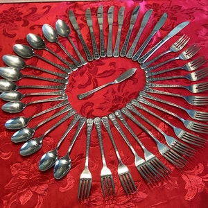 Könnte beinhalten: Ein Besteckset, das in einem Kreis auf einer roten Tischdecke angeordnet ist. Das Set enthält Löffel, Gabeln und Buttermesser.