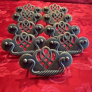 May include: Ten antique-style cabinet knobs with a decorative, intricate design. The knobs are made of metal and have a dark, aged finish.