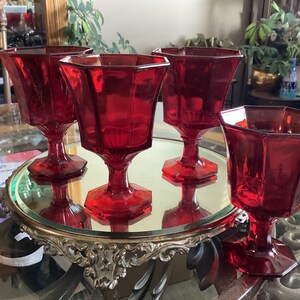 May include: Set of four red glass goblets with a faceted design. The goblets are on a silver tray with a mirrored surface.