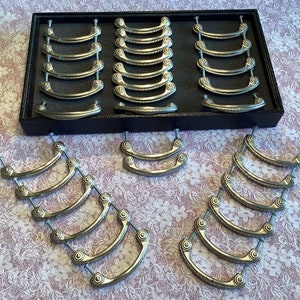 May include: A set of 20 silver drawer pulls with a decorative design. The pulls are arranged in a black box with a velvet lining.