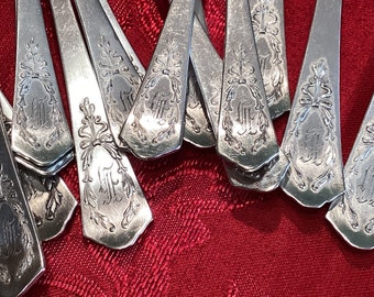 May include: A close-up of a set of silver spoons with ornate handles. The handles are decorated with a floral design and a monogram.