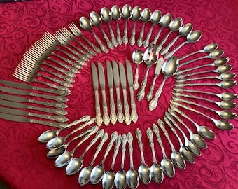 Könnte beinhalten: Eine Anordnung von Vintage-Besteck auf einer roten Tischdecke. Das Set umfasst Gabeln, Messer und verschiedene Löffelgrößen, einschließlich Servierlöffel. Das Besteck hat verzierte Griffe und eine polierte Oberfläche.