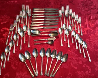 May include: A set of silver flatware, including forks, knives, and spoons, arranged on a red tablecloth. The flatware has an ornate design with a floral pattern.