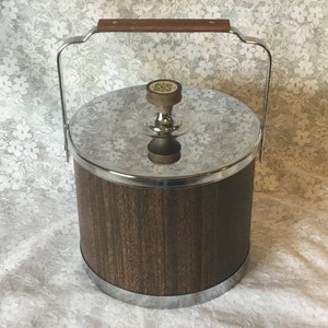 May include: A brown and silver ice bucket with a wooden lid and a chrome handle. The lid has a small knob on top.
