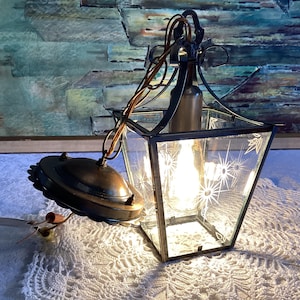 Może przedstawiać: Winylowa lampa sufitowa z szkła i metalu z wzorem gwiazdy na szkle. Lampa jest zawieszona na łańcuchu i ma jedną żarówkę.