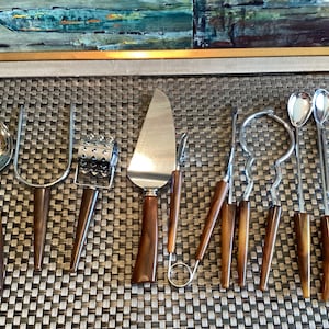 May include: A set of ten stainless steel kitchen utensils featuring brown marbled handles. The collection includes a slotted spoon, a two-pronged fork, a rotary grater, a cake server, a small knife, and various specialised serving tools.