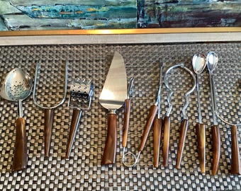 Op de afbeelding: Een set van tien roestvrijstalen keukengerei met bruin gemarmerde handvatten. De collectie bevat een schuimspaan, een vork met twee tanden, een roterende rasp, een taartschep, een klein mes en diverse gespecialiseerde serveergereedschappen.