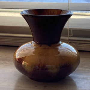 May include: A brown and gold ceramic vase with a flared top and a rounded body. The vase has a glossy finish.
