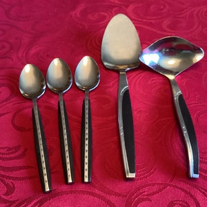 以下が含まれることがあります： 黒いハンドルが付いた銀色のサービング食器5点セット。セットにはスプーン3本、サービングスプーン1本、レードル1本が含まれています。
