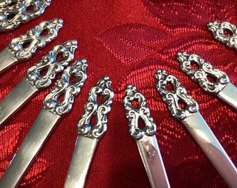 May include: Close-up of a set of silver-plated teaspoons with ornate, decorative handles. The handles are intricately designed with swirls and loops, creating a delicate and elegant look.