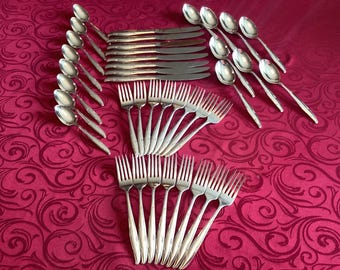 May include: A set of silverware, including forks, knives, and spoons, arranged in a fan shape on a red tablecloth with a swirling pattern. The silverware is made of polished silver and has a classic design.