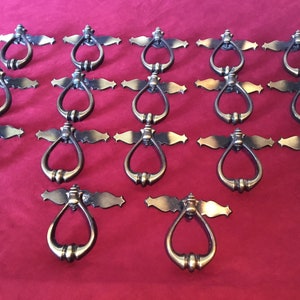 以下が含まれることがあります： 装飾的な華やかなデザインのアンティークブラス製のキャビネットドアプル18個セット。各プルには、涙滴型のベースにリング型のハンドルが付いています。