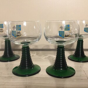 May include: Four clear glass wine glasses with green stems and bases. Each glass has a gold and blue crest with the text "WURZBURG 1980" and a compass rose.