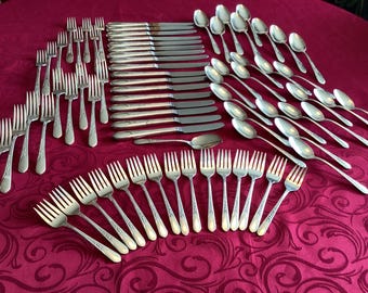 May include: A set of silverware, including forks, knives, and spoons, laid out on a red tablecloth. The silverware is made of polished silver and has an ornate design.
