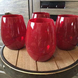 May include: Four red glass tumblers on a wooden table with a metal rim. The tumblers are round and have a smooth, shiny surface.